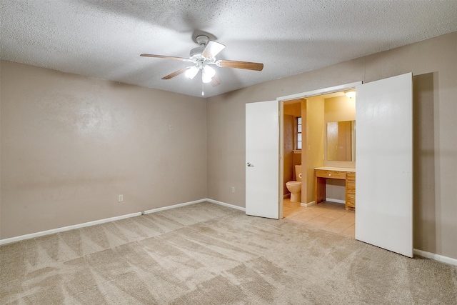 unfurnished bedroom featuring built in desk, ensuite bath, a textured ceiling, light colored carpet, and ceiling fan