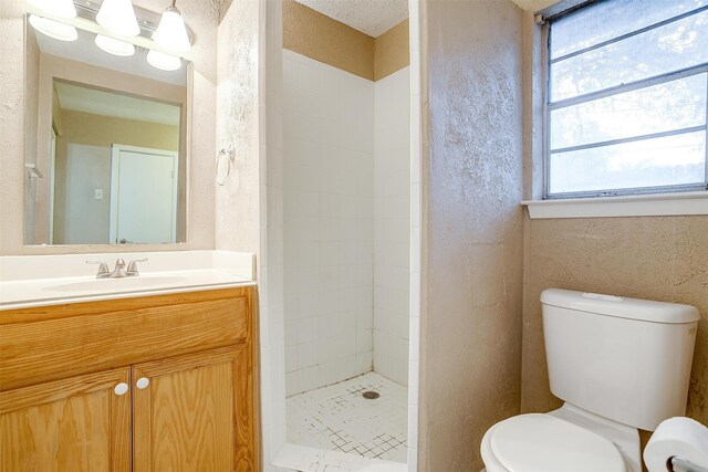 bathroom with vanity, a textured ceiling, toilet, and a tile shower