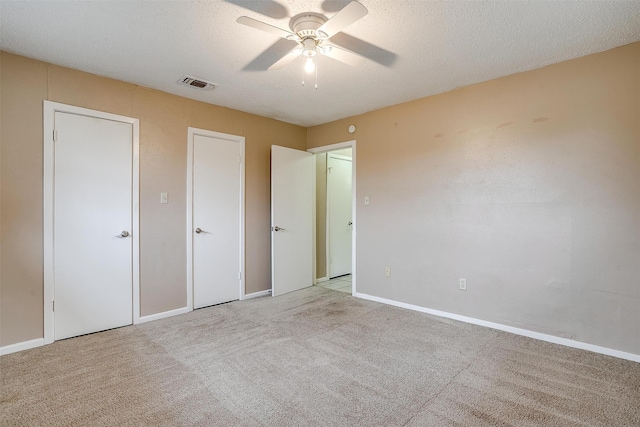 unfurnished bedroom featuring two closets, a textured ceiling, light carpet, and ceiling fan