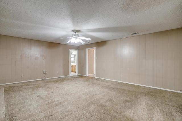 carpeted spare room with wood walls, a textured ceiling, and ceiling fan