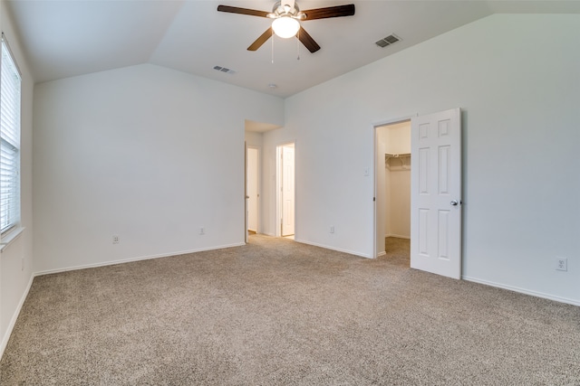 unfurnished bedroom featuring a walk in closet, lofted ceiling, carpet, and ceiling fan