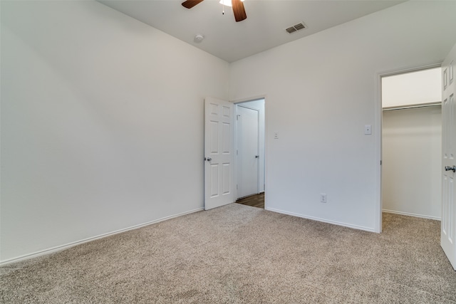 unfurnished bedroom featuring a closet, a walk in closet, carpet flooring, and ceiling fan