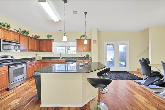 kitchen featuring stainless steel appliances, sink, dark stone countertops, a center island, and light wood-type flooring