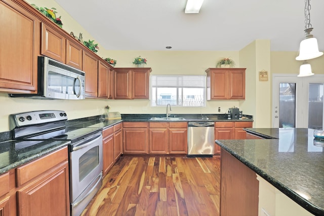 kitchen with dark stone counters, appliances with stainless steel finishes, pendant lighting, sink, and hardwood / wood-style flooring