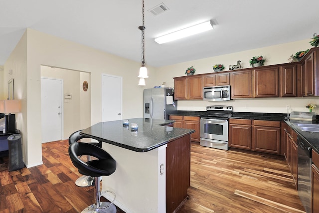 kitchen featuring appliances with stainless steel finishes, a kitchen bar, hardwood / wood-style floors, a kitchen island, and pendant lighting