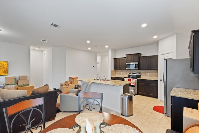 kitchen featuring dark brown cabinetry, sink, light stone counters, appliances with stainless steel finishes, and tasteful backsplash