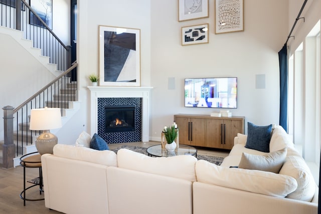 living room with a high ceiling, a tile fireplace, and light hardwood / wood-style flooring