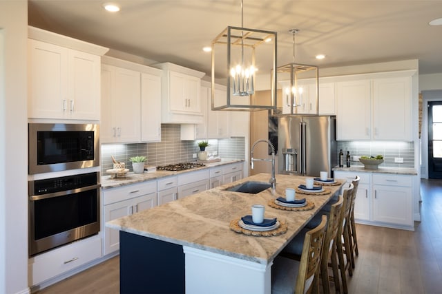 kitchen with white cabinets, stainless steel appliances, sink, and an island with sink