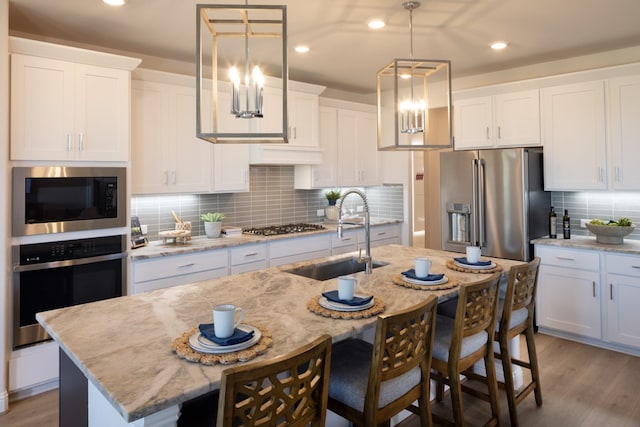 kitchen with stainless steel appliances, hanging light fixtures, white cabinets, and an island with sink