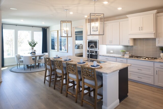 kitchen with dark wood-type flooring, white cabinets, decorative light fixtures, and a kitchen island with sink