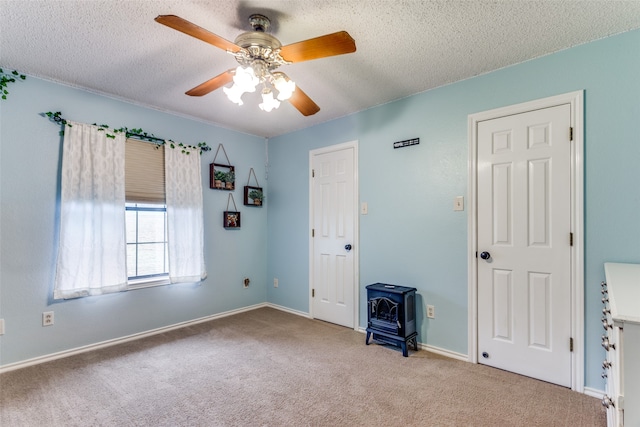 empty room featuring a textured ceiling, ceiling fan, a wood stove, and light carpet