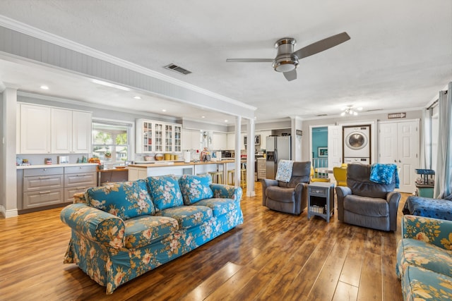 living room with a textured ceiling, hardwood / wood-style flooring, ceiling fan, crown molding, and stacked washer / drying machine