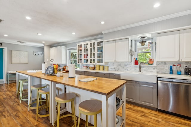 kitchen featuring butcher block counters, white cabinetry, sink, stainless steel dishwasher, and light wood-type flooring