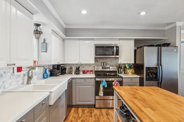 kitchen featuring butcher block counters, white cabinetry, appliances with stainless steel finishes, light hardwood / wood-style flooring, and crown molding