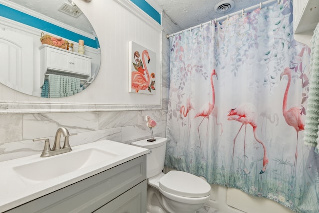 bathroom with a textured ceiling, vanity, crown molding, toilet, and tile walls