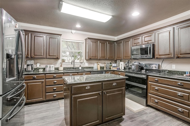 kitchen with sink, ornamental molding, appliances with stainless steel finishes, dark brown cabinets, and a kitchen island