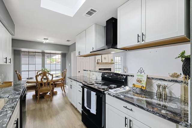 kitchen featuring white cabinetry, light wood-type flooring, black appliances, and wall chimney range hood