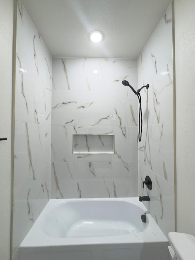 bathroom with tiled shower / bath combo, toilet, and a textured ceiling