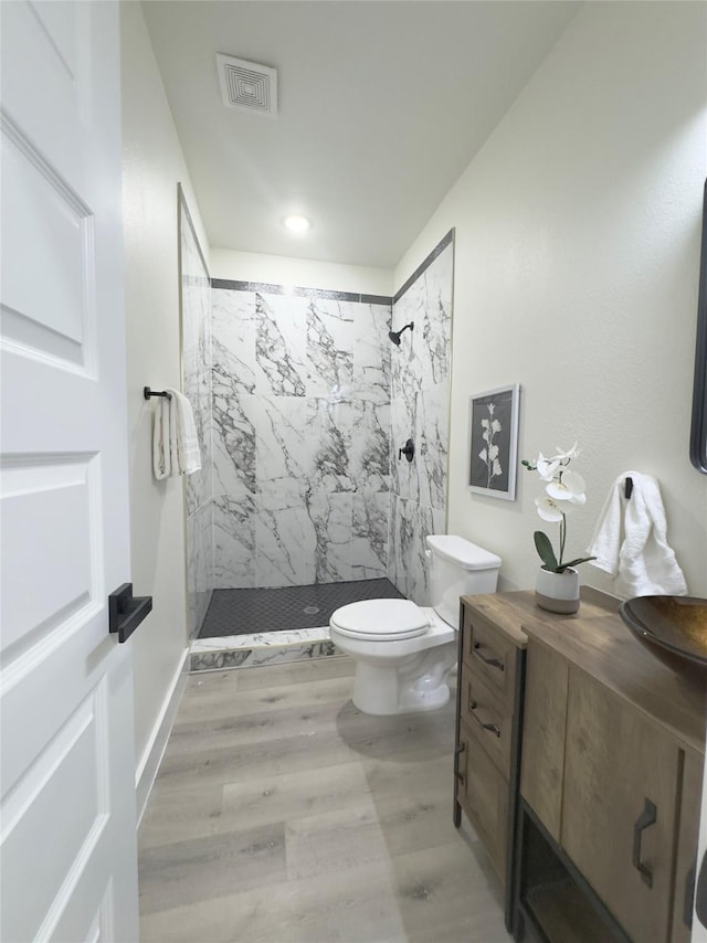 bathroom with hardwood / wood-style flooring, toilet, sink, and tiled shower