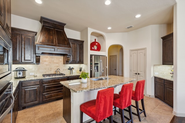 kitchen featuring premium range hood, sink, a kitchen island with sink, a kitchen breakfast bar, and stainless steel appliances