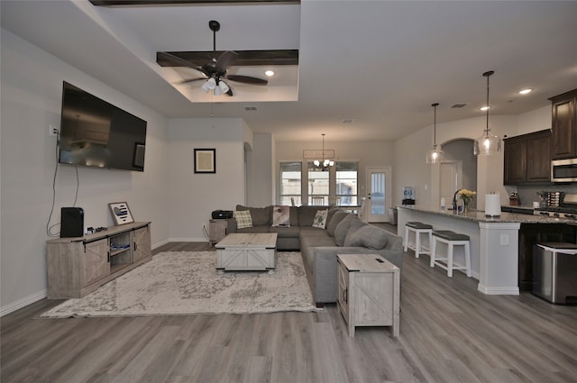 living room with ceiling fan with notable chandelier, sink, light wood-type flooring, and a raised ceiling