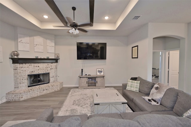 living room with hardwood / wood-style floors, ceiling fan, a tray ceiling, and a brick fireplace