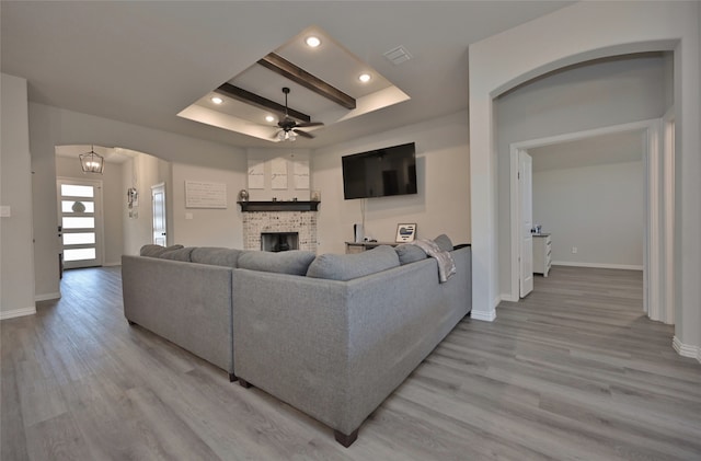 living room featuring a fireplace, ceiling fan, light hardwood / wood-style floors, and beam ceiling