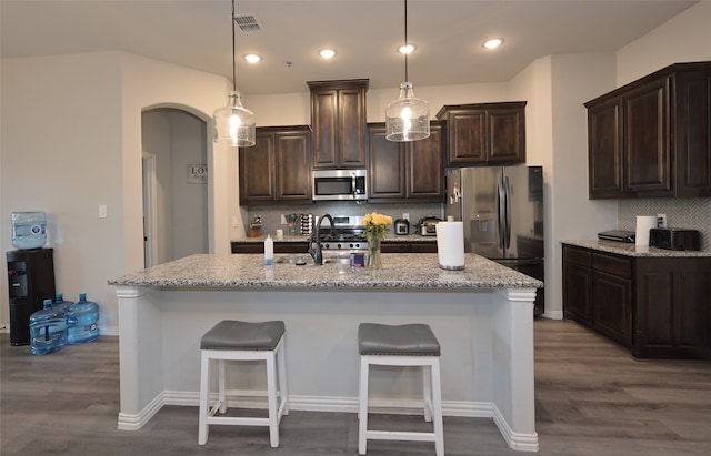 kitchen featuring light stone countertops, appliances with stainless steel finishes, a center island with sink, and dark hardwood / wood-style floors