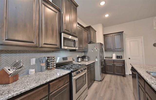 kitchen featuring dark brown cabinetry, appliances with stainless steel finishes, light hardwood / wood-style floors, and light stone countertops