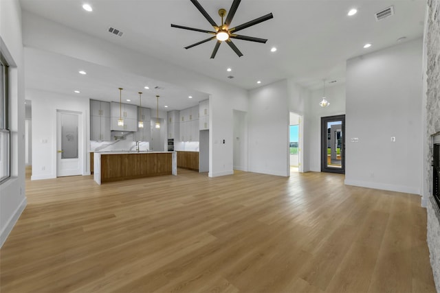 unfurnished living room featuring ceiling fan with notable chandelier, light hardwood / wood-style flooring, and a high ceiling