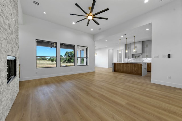 unfurnished living room featuring ceiling fan, light hardwood / wood-style floors, and a stone fireplace