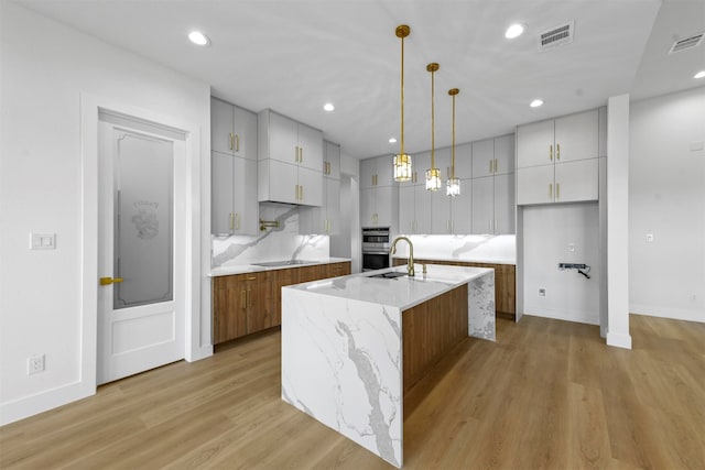 kitchen featuring pendant lighting, an island with sink, light stone countertops, and light hardwood / wood-style flooring