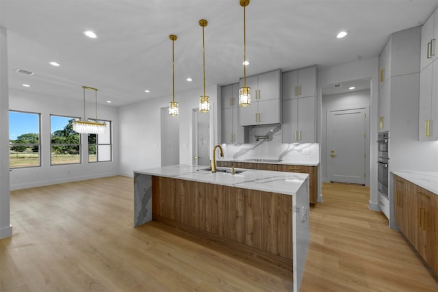 kitchen with light stone counters, sink, a spacious island, light hardwood / wood-style flooring, and decorative light fixtures