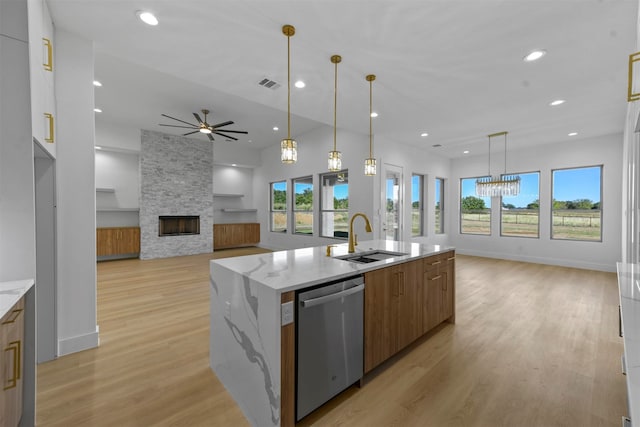 kitchen with a center island with sink, sink, stainless steel dishwasher, a fireplace, and light wood-type flooring