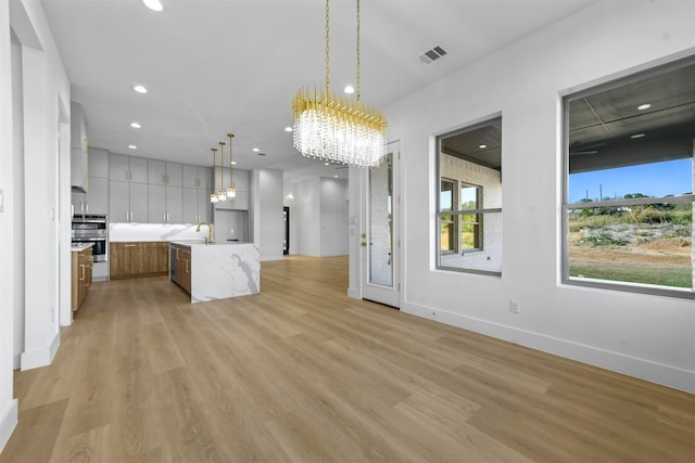 kitchen featuring stainless steel double oven, pendant lighting, light hardwood / wood-style floors, and a kitchen island with sink