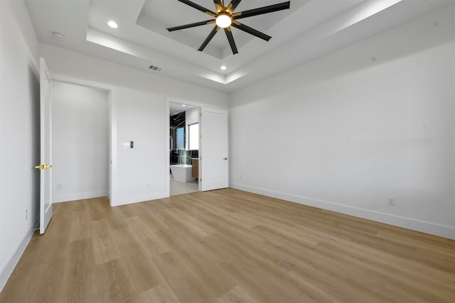 unfurnished bedroom with ensuite bath, ceiling fan, light hardwood / wood-style floors, and a raised ceiling