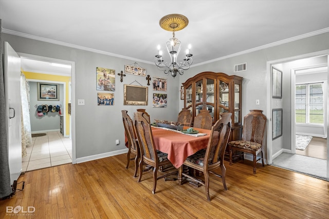 dining area with light wood-type flooring, ornamental molding, and an inviting chandelier