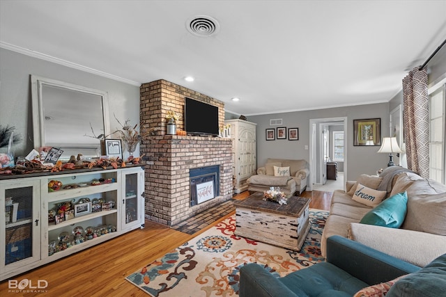 living room with light hardwood / wood-style floors, ornamental molding, and a brick fireplace