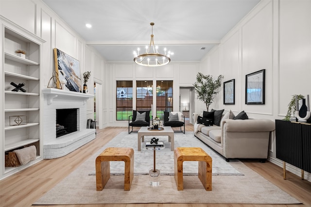 living room featuring a brick fireplace, light hardwood / wood-style floors, built in features, and an inviting chandelier