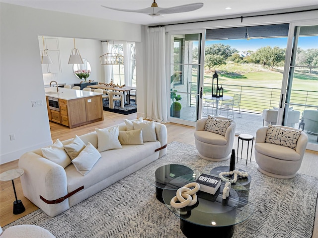 living area featuring light wood-type flooring, baseboards, and ceiling fan with notable chandelier