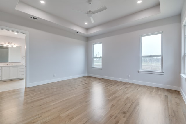 spare room with a tray ceiling, light hardwood / wood-style flooring, and ceiling fan