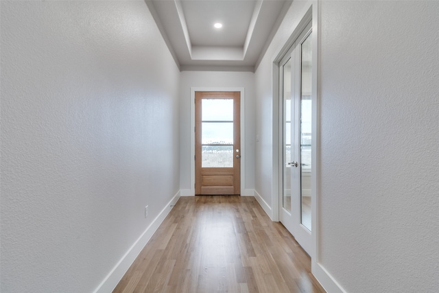 entryway with light hardwood / wood-style floors and a raised ceiling