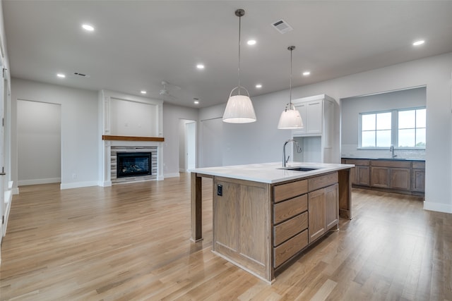 kitchen with sink, pendant lighting, light hardwood / wood-style floors, a kitchen island with sink, and a breakfast bar