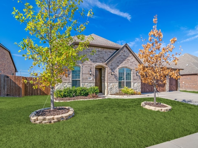 french country home featuring a garage, brick siding, fence, concrete driveway, and a front lawn