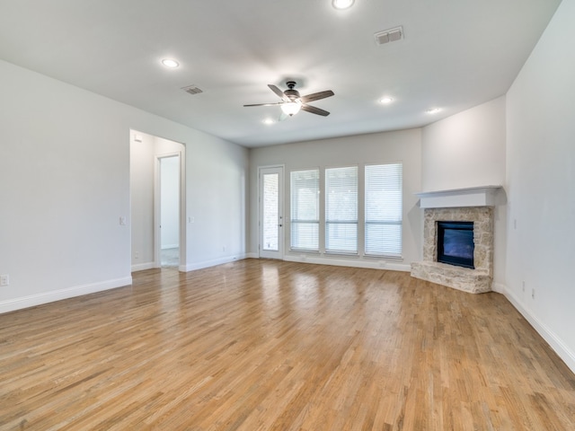 unfurnished living room with ceiling fan, light hardwood / wood-style floors, and a stone fireplace