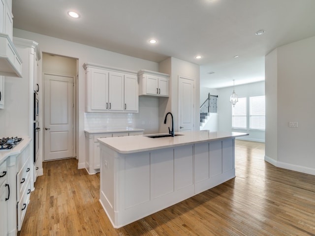 kitchen featuring white cabinets, sink, a kitchen island with sink, and light hardwood / wood-style flooring