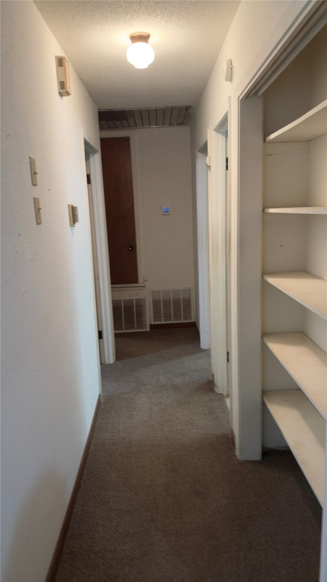 hall featuring a textured ceiling and dark colored carpet