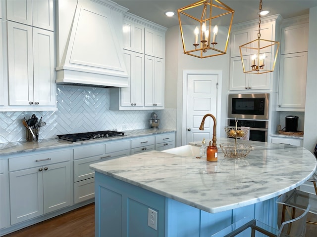 kitchen featuring white cabinetry, hanging light fixtures, stainless steel appliances, premium range hood, and a center island with sink