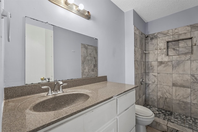 bathroom featuring tiled shower, vanity, a textured ceiling, and toilet