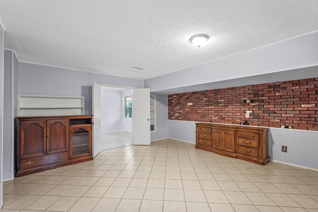 unfurnished living room featuring light tile patterned floors, a textured ceiling, and brick wall